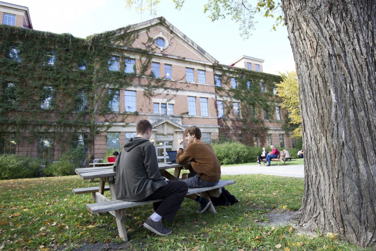 Two students with a laptop sit at a picnic table in front of the Engineering Building