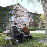 Two students with a laptop sit at a picnic table in front of the Engineering Building