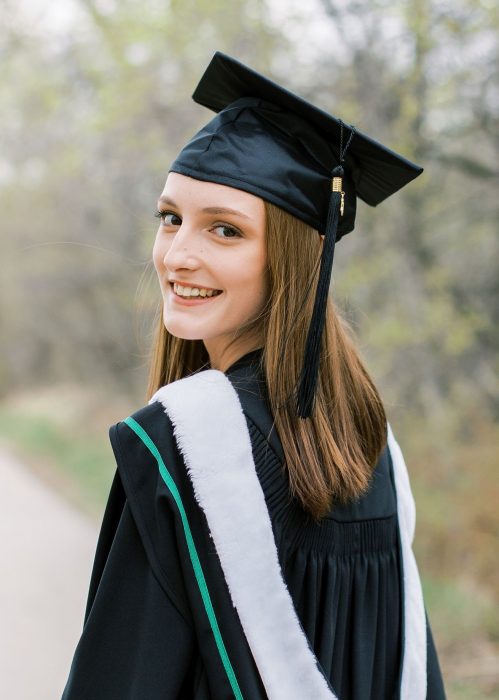 woman wearing graduation cap and gown looking back over her shoulder