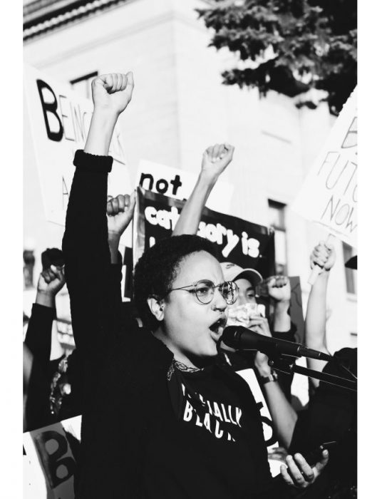 black and white photo of a black woman with fist raised, passionately speaking at a rally