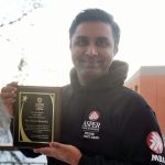 Man with dark hair holding a plaque in a black Asper School of Business hoodie.