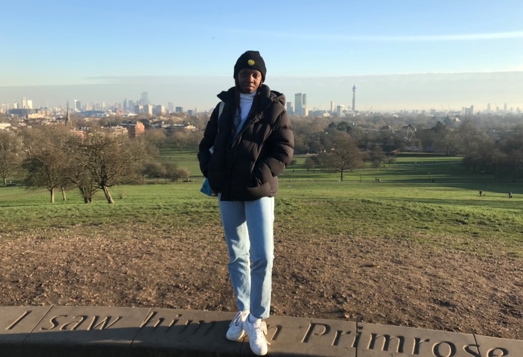 woman in parka and toque standing, with city landscape behind her