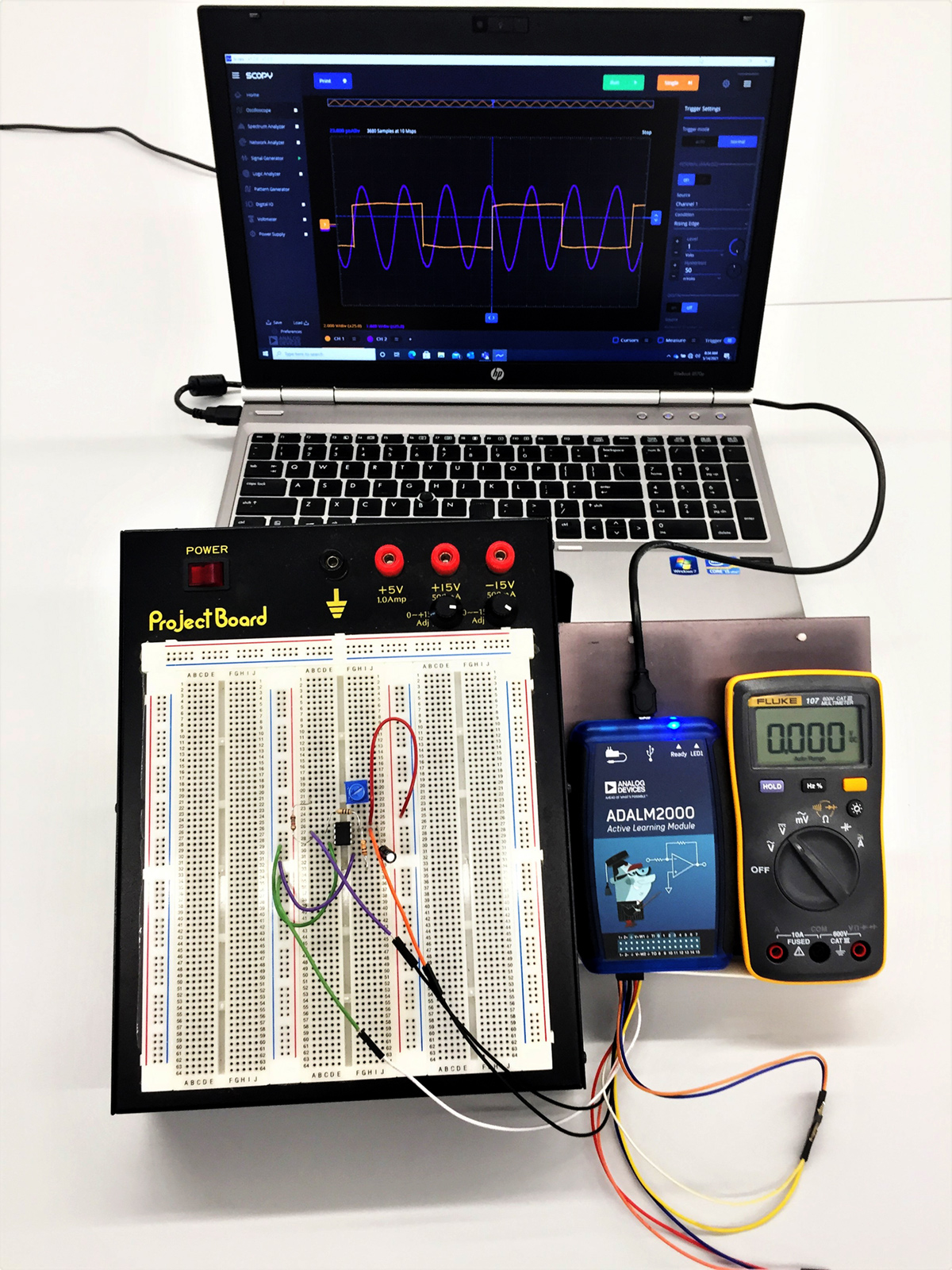 The typical setup of the at-home lab kit in use with a laptop computer. The ADALM2000 interfaces with the software on the laptop computer to allow students to generate signals and make measurements of the lab circuits which provide real-time data to compare with the simulation data set.