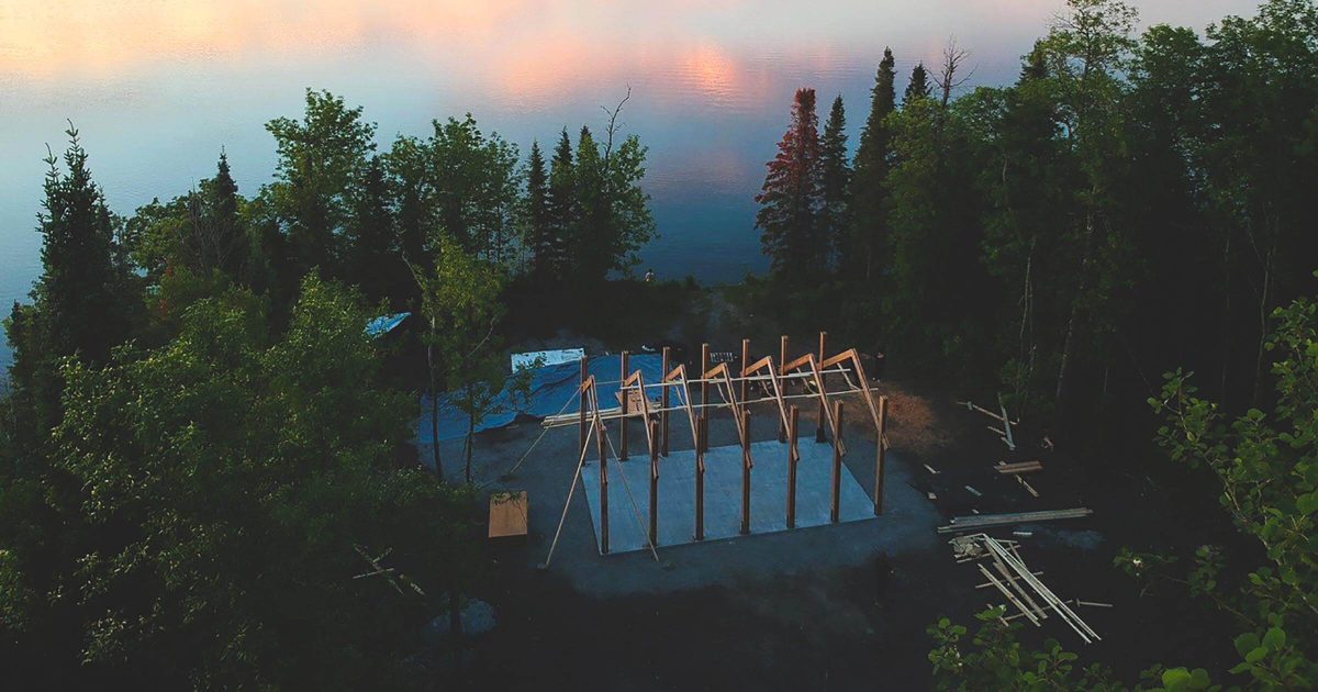 An aerial photo of a building being constructed on treed land near a lake.