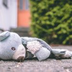 A stuffed teddybear lies face down on pavement.