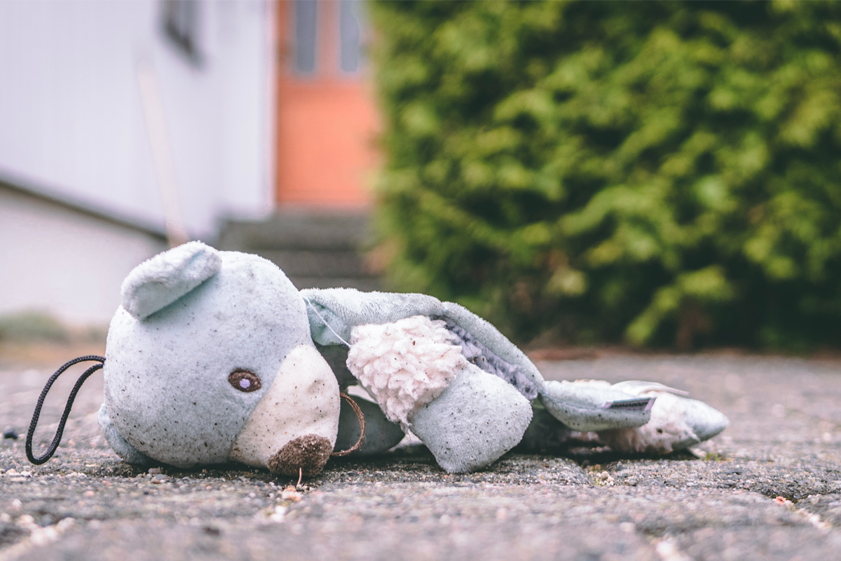 A stuffed teddybear lies face down on pavement.
