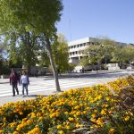 Students walking by University Centre with yellow flowers in the foreground