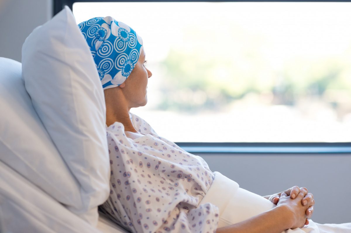 A female cancer patient looks out a window while propped up in a hospital bed.