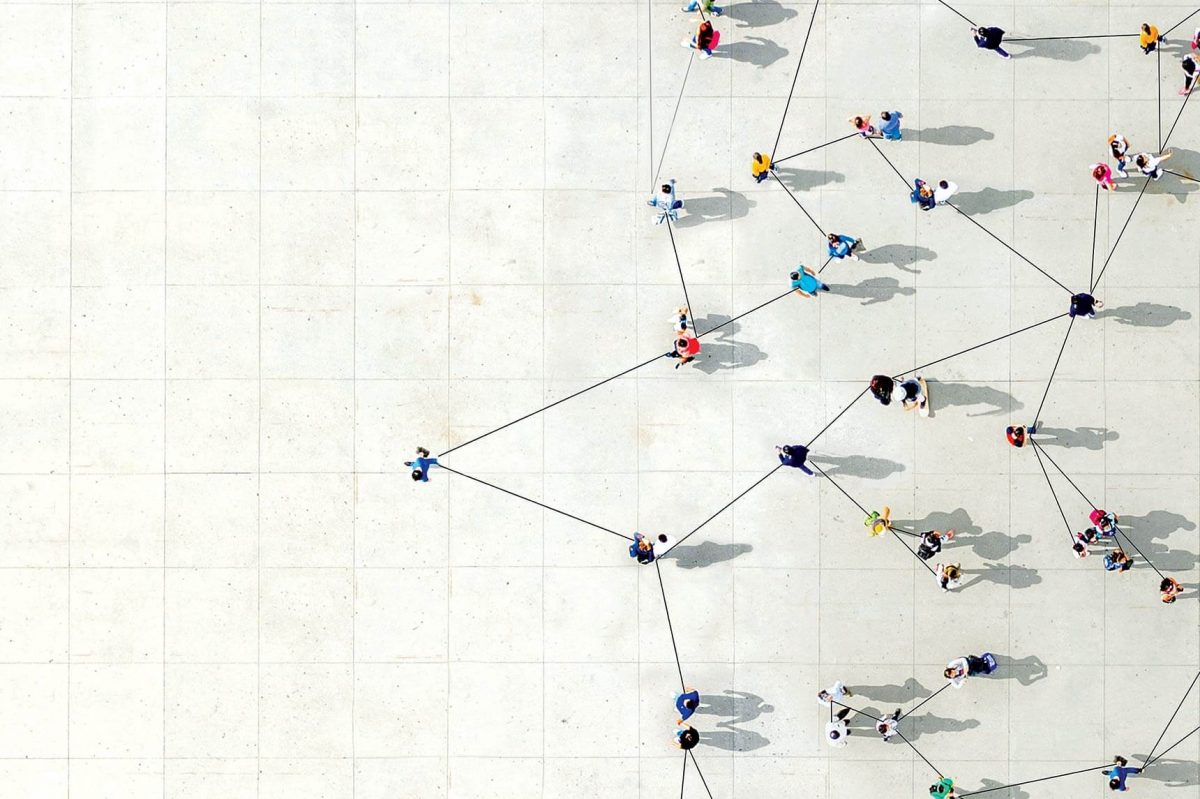 An overhead view of people standing in a crowd, all connected by interlinked strings.