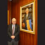 Dr. Brian Hennen stands beside a painted portrait of himself that hangs on a paneled wall.