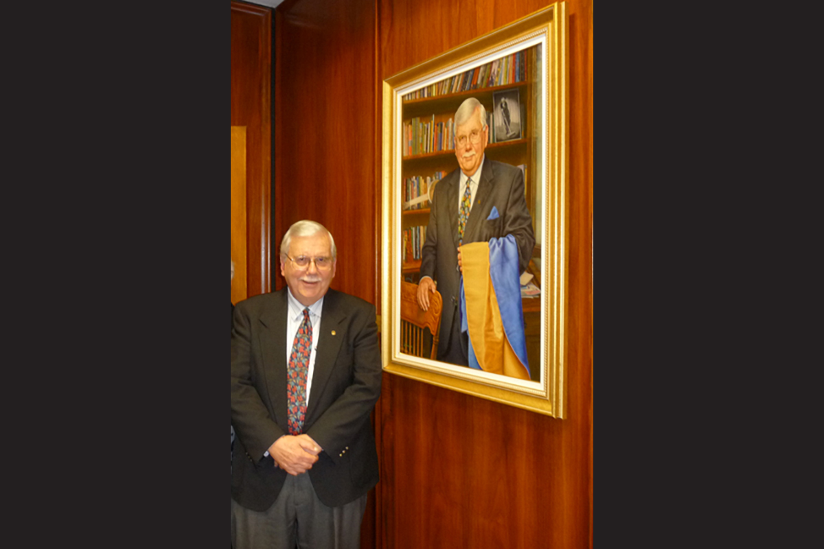 Dr. Brian Hennen stands beside a painted portrait of himself that hangs on a paneled wall.