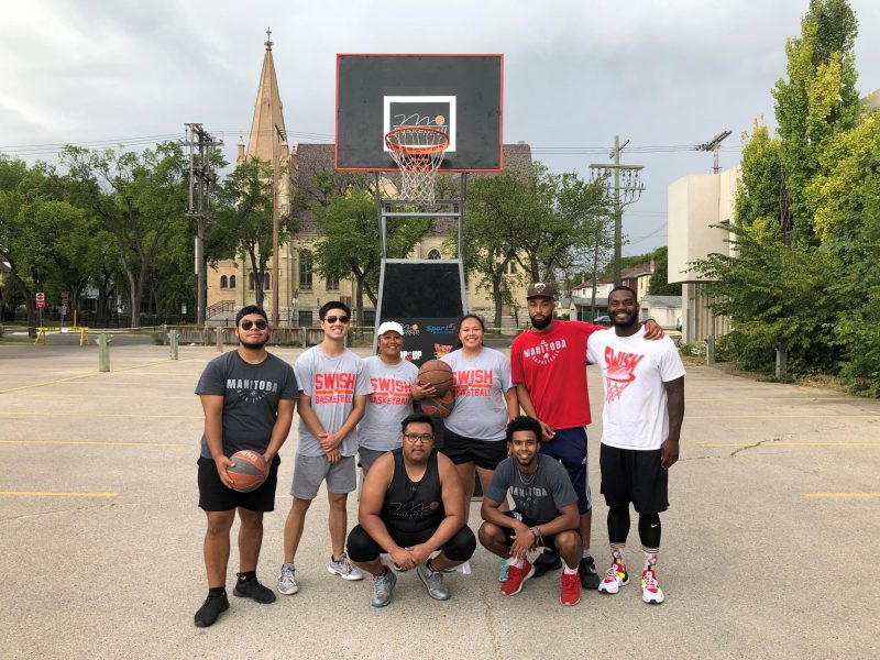 Eight SWISH staff members pose for a photo beneath a basketball hoop outside.