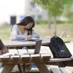 masked student seated at outdoor picnic table