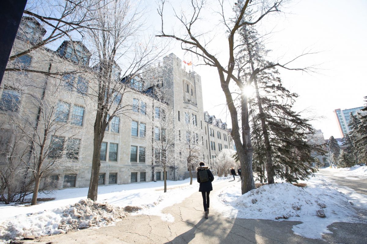 A student walks alone on campus during the winter, heading towards a white brick building.