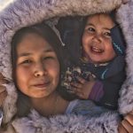 The faces of an Inuit mother and toddler are encircled by the fur of her parka hood.
