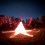 teepee bathed in orange spotlights with a night sky