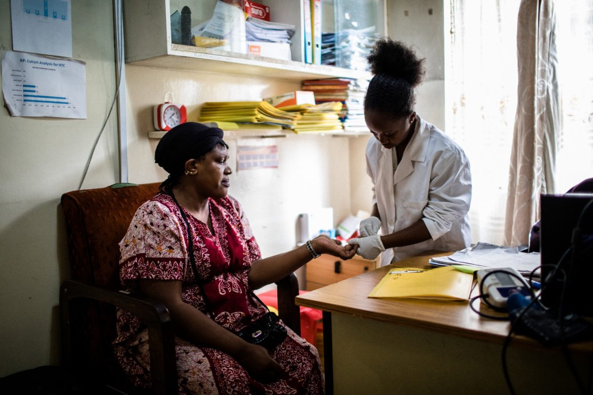 At a clinic in Nairobi, Kenya, a nurse or doctor examines the hand of a seated patient.