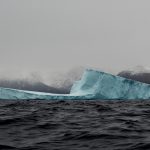 an iceberg in open water with hazy clouds surrounding it