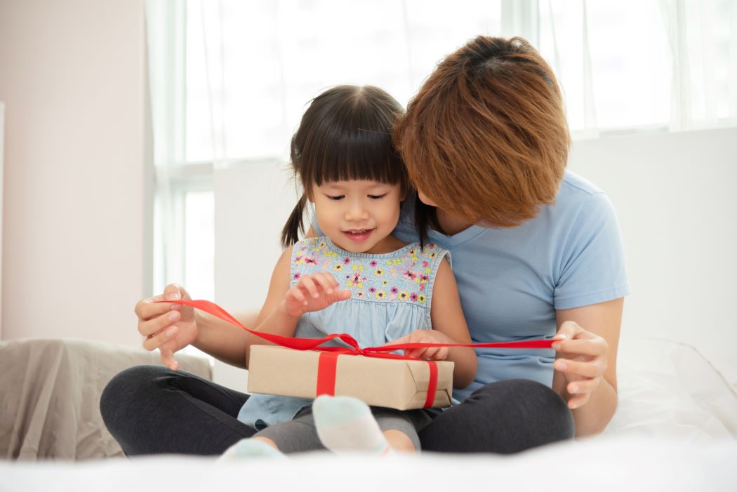 A mother helps a child open a gift.