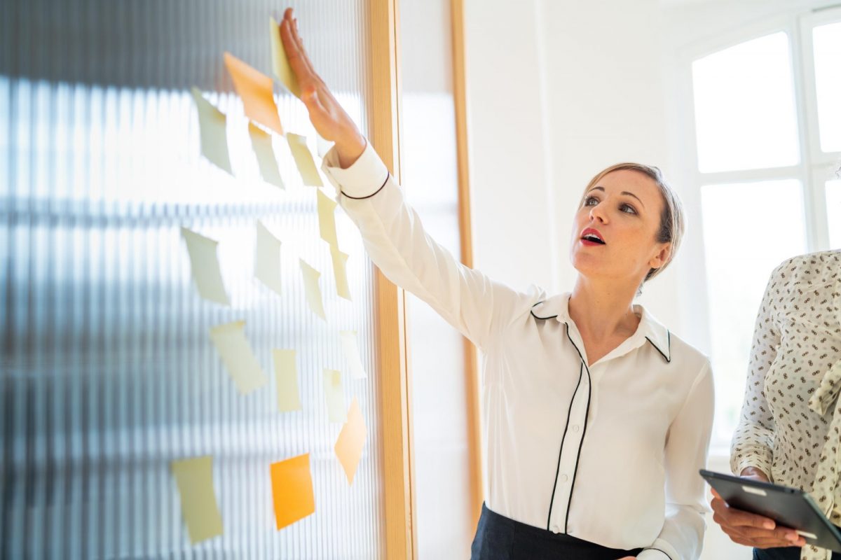 Woman in white collar shirt putting sticky notes on a board for an Asper School of Business Executive Education photo.