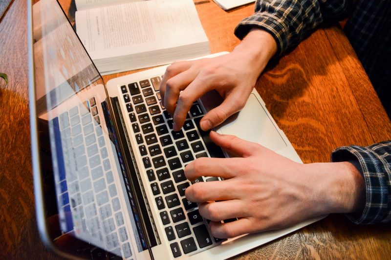 a student's hands type on a laptop. School books sit on the desk in the background.