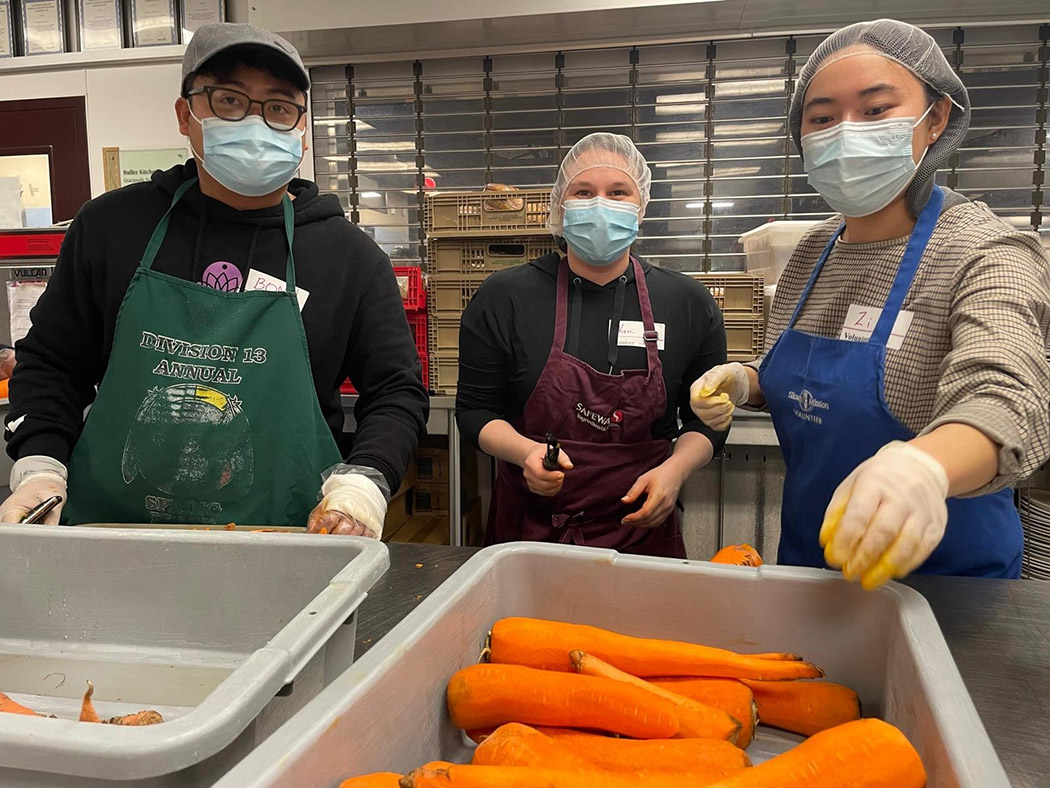 Three students in masks volunteering in a kitchen.