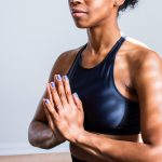 A feminine person sits meditating on a yoga mat with their hands pressed together