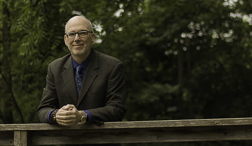 Professor Thomas Telfer leaning on a wood rail with a forest background