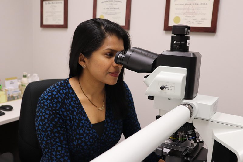 Dr. Vimi Mutalik peers into a large microscope on her office desk.