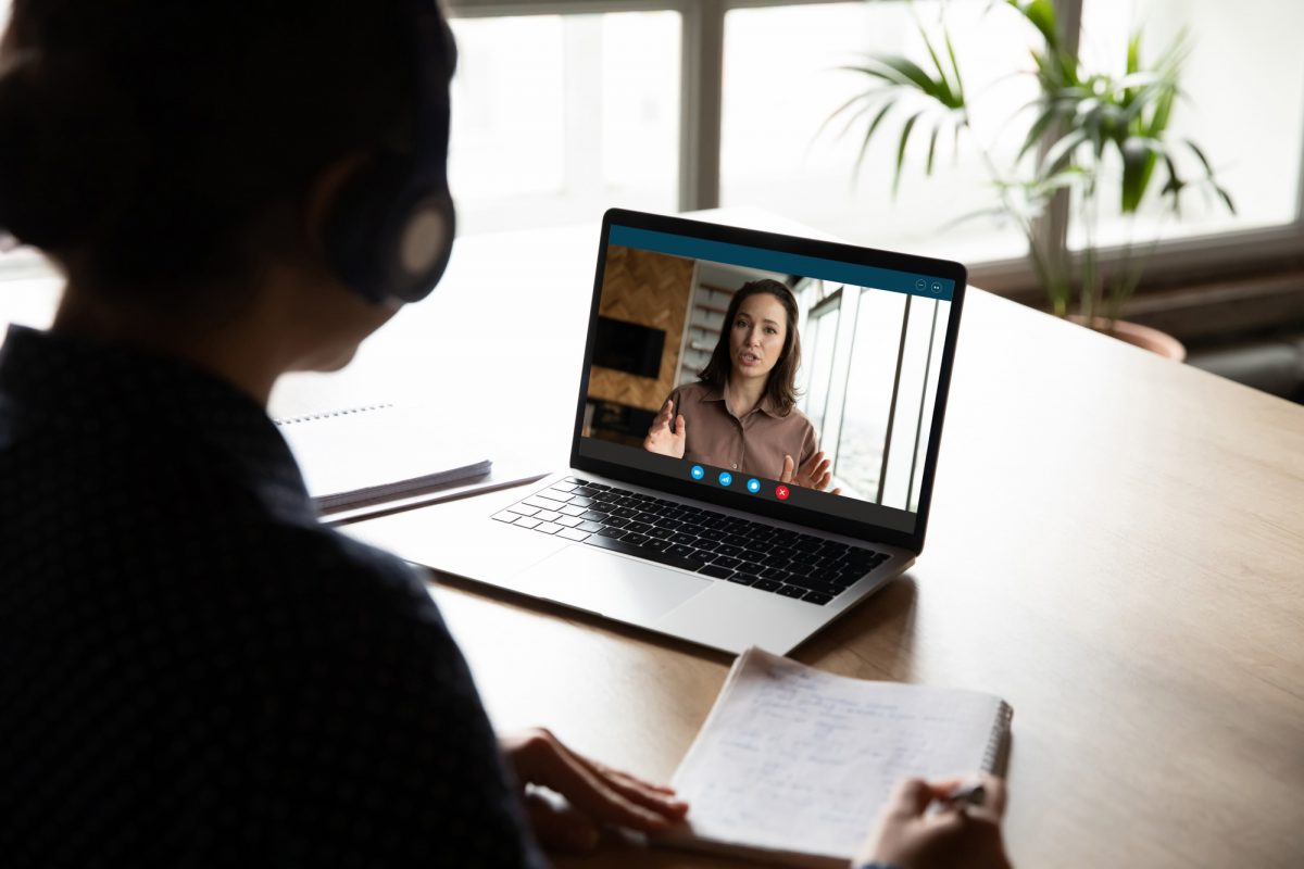 person with headphones on looking at laptop screen where woman is online chatting