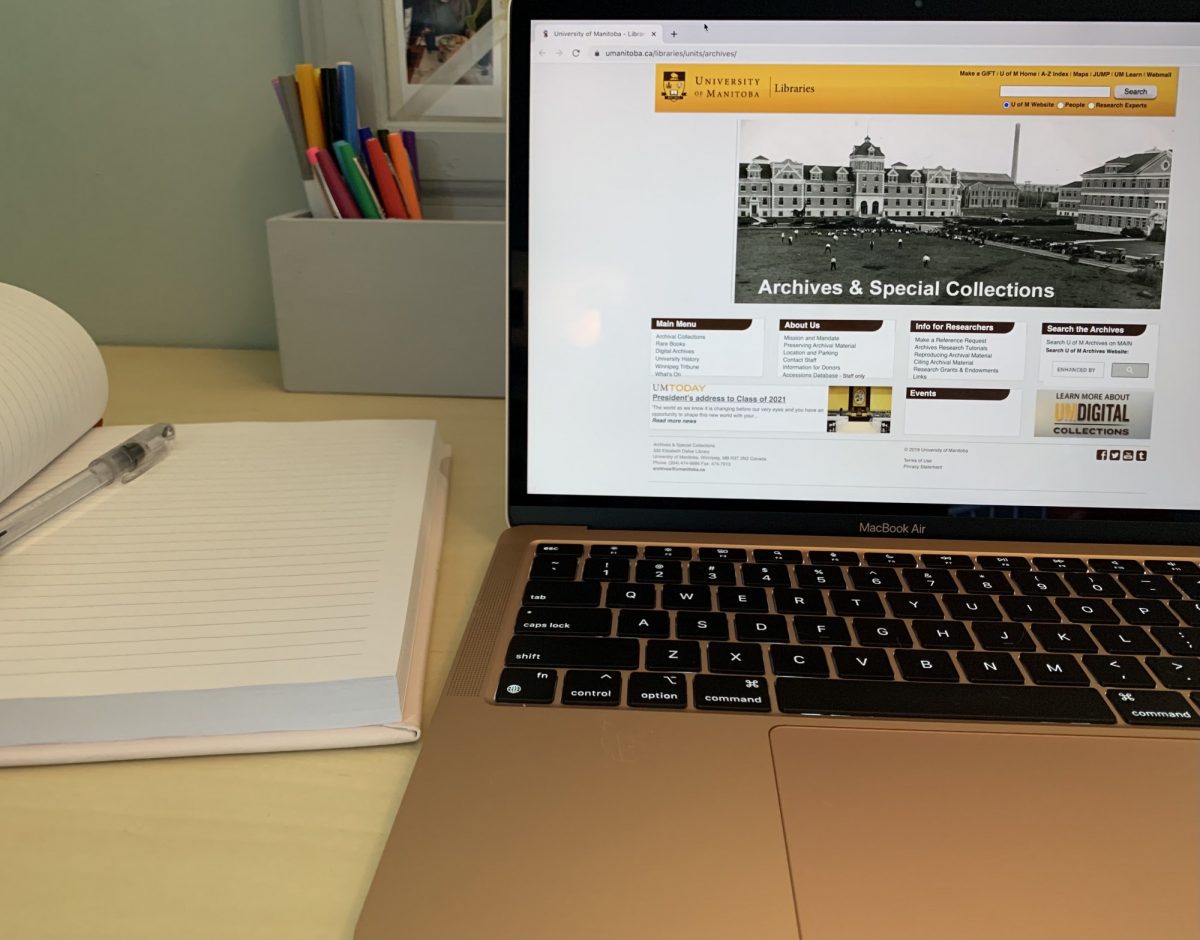 desk with a open notebook and open laptop. the screen is open to athe university of manitoba libraries webpage.