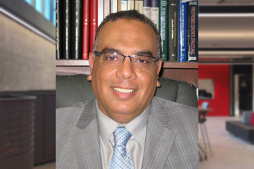 A professional photo of Ehab El-Salakawy sitting, posing and smiling for the camera in front of a book shelf.