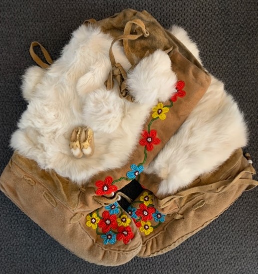 Traditional leather Moccasins with white fur and colourful beaded flowers on a grey background.