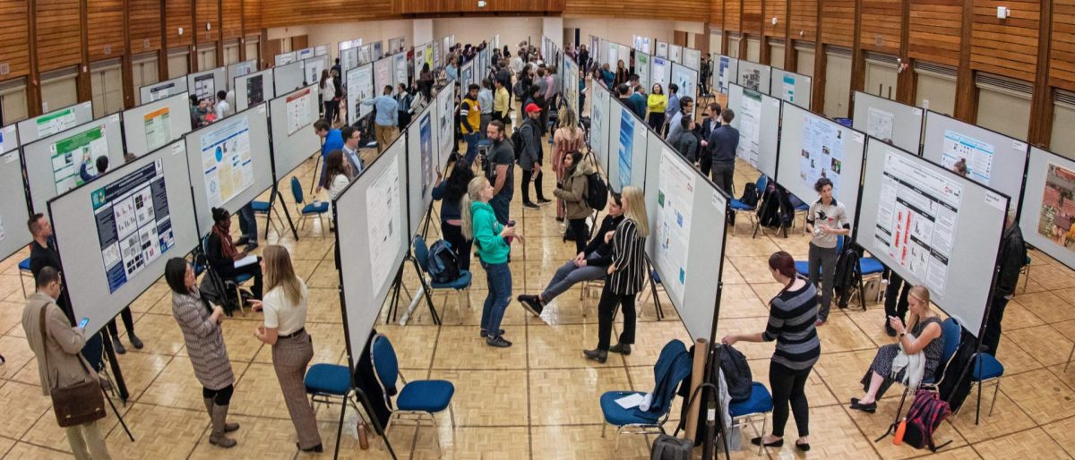 side angle shot of students standing in front of their research posters in an auditorium