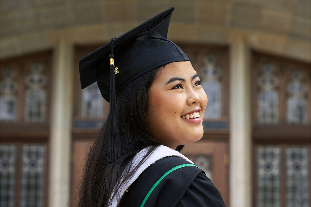 A woman in convocation attire smiles as she looks off into the distance.