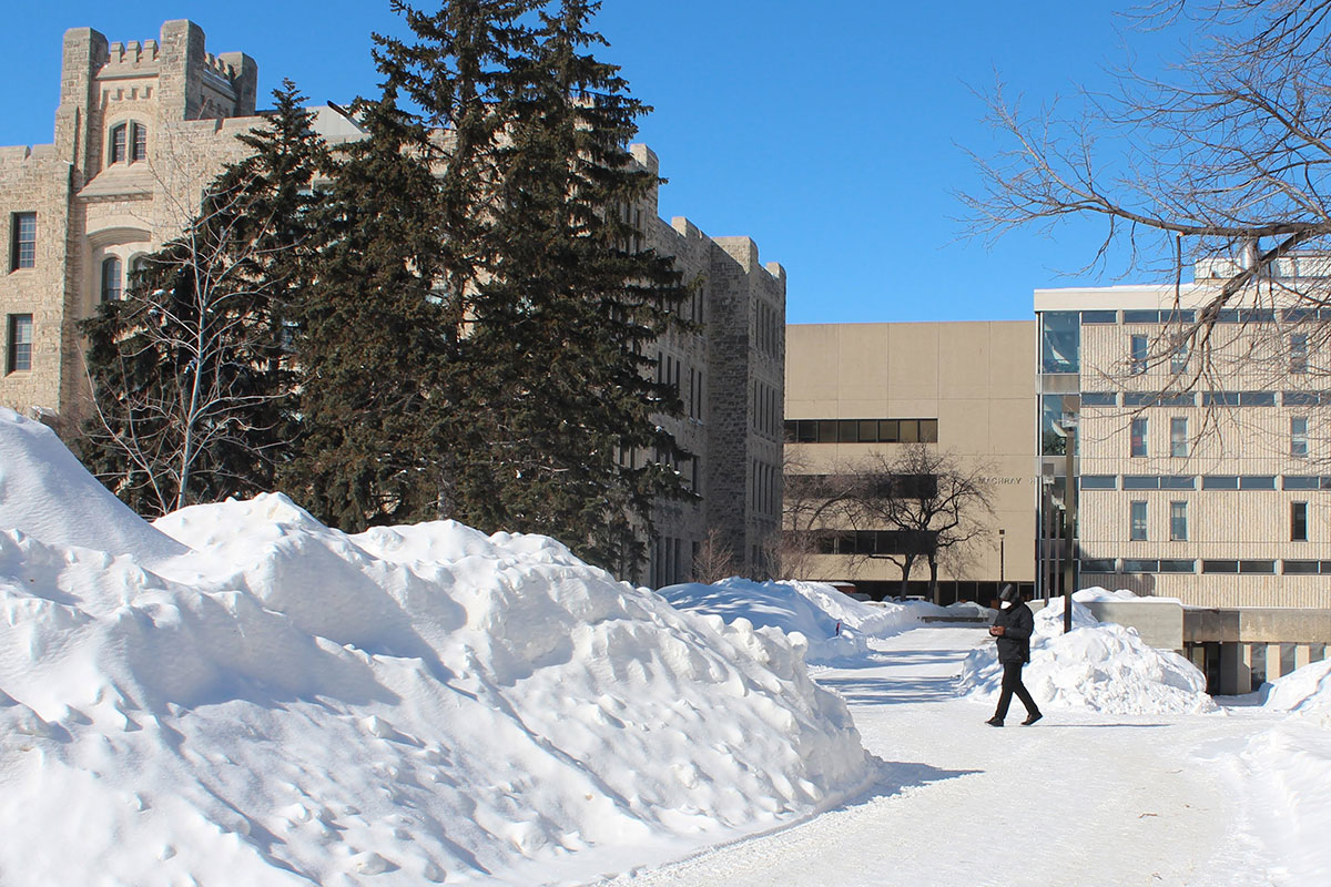 A person wearing a mask walks on Fort Garry campus in winter 2022. // Photo by Jack Rach