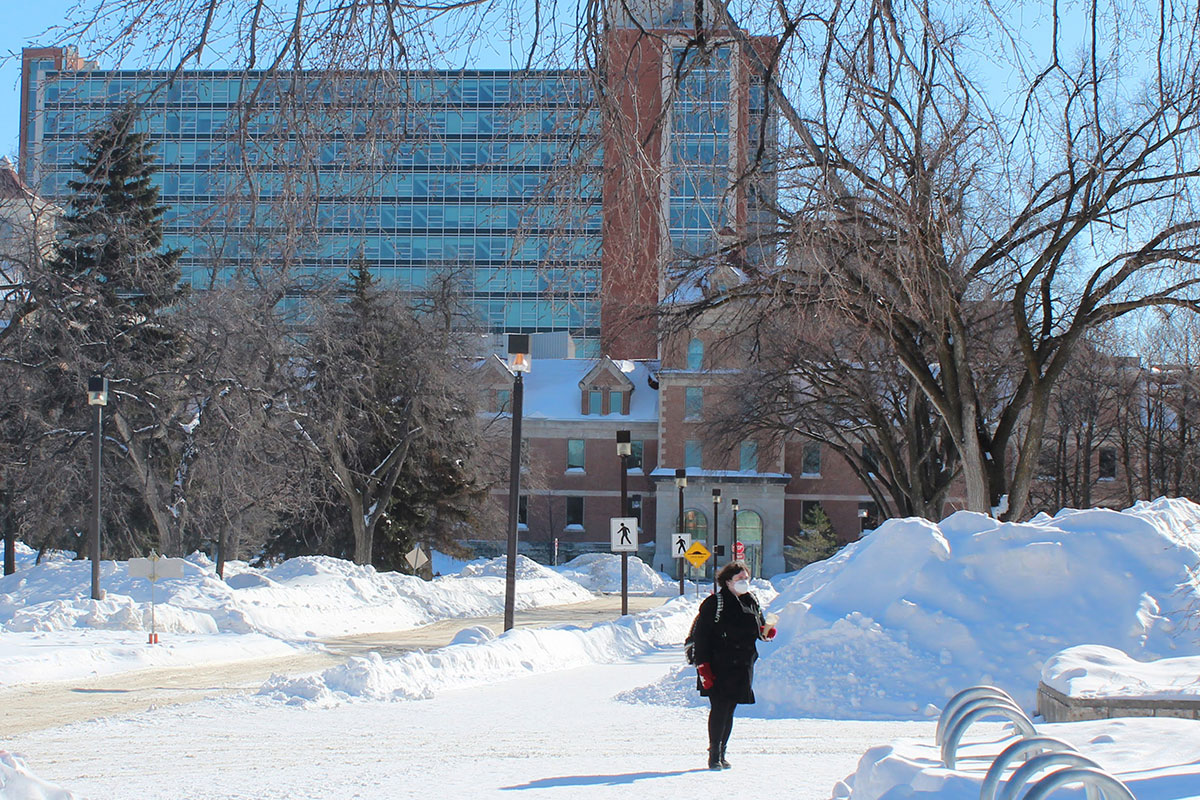 Person wearing mask walks on Fort Garry campus in winter 2022. // Photo by Jack Rach