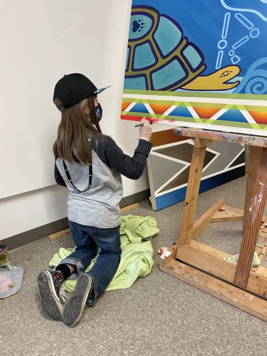 A young boy wearing a hat paints the corner of a mural