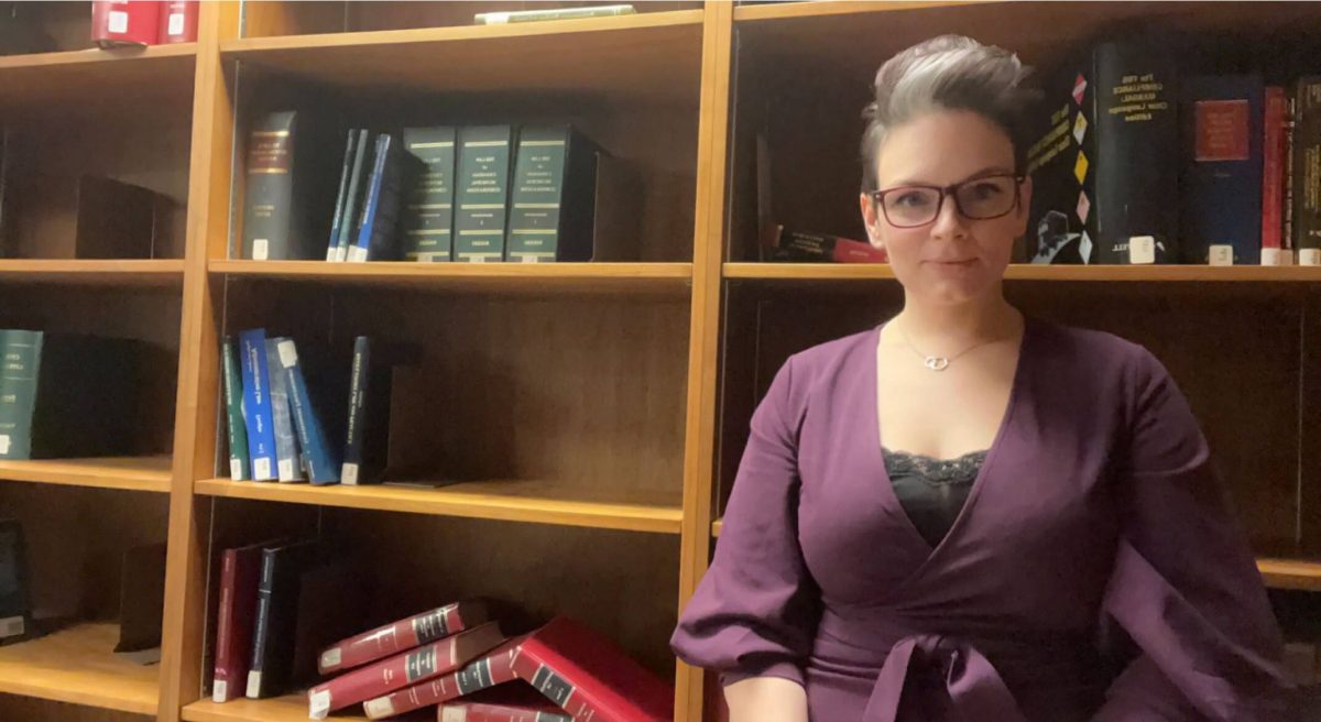 Student stands in front of bookcase.