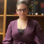 Student stands in front of bookcase.