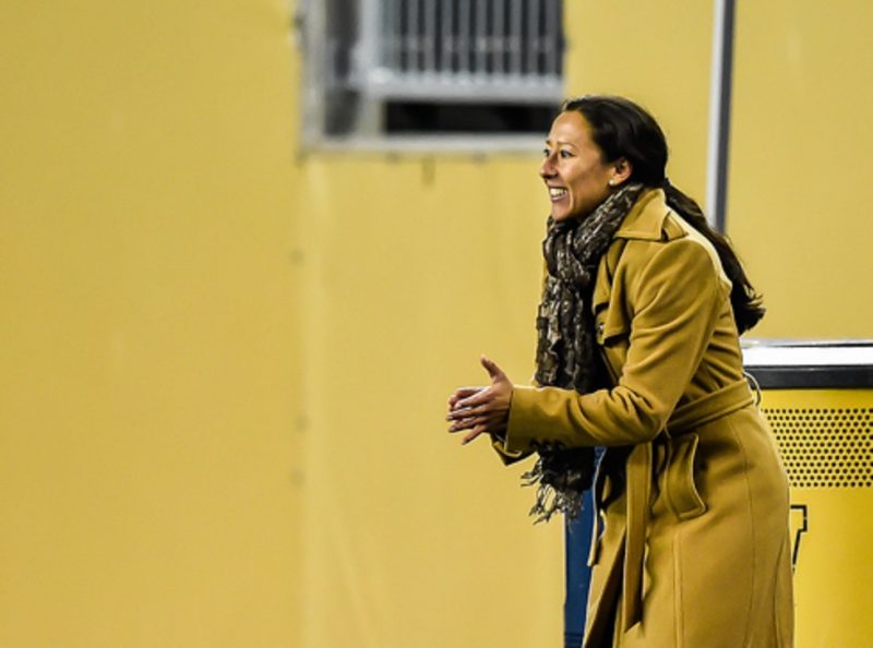 Vanessa Martinez, wearing a coach, stands on the sidelines of a game