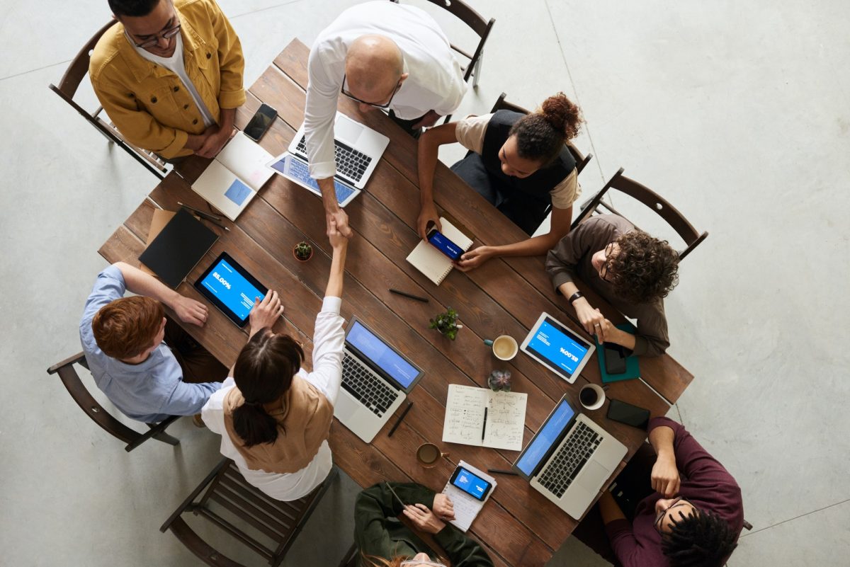 Eight business people collaborating around a table, each with a mobile device.