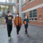 Three students with masks on walking through the Engineering building atrium.