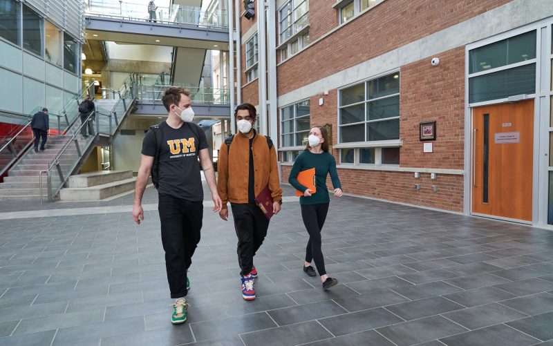 Three students with masks on walking through the Engineering building atrium.