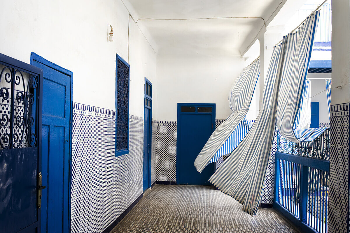 A photo in which blue curtains blow in the wind in an empty synagogue hall.