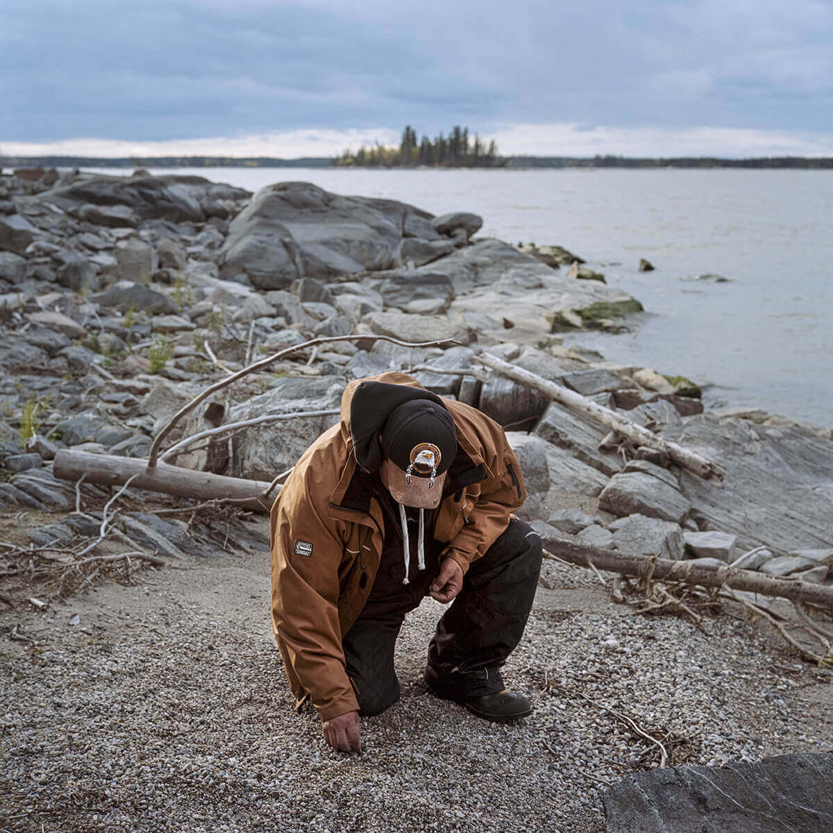 A photo of an Indigenous man kneeling on a shoreline.