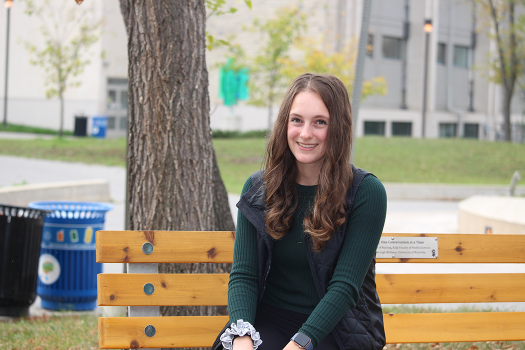 Student Gillian Laninga sits on a bench outside the College of Nursing building at Fort Garry Campus.