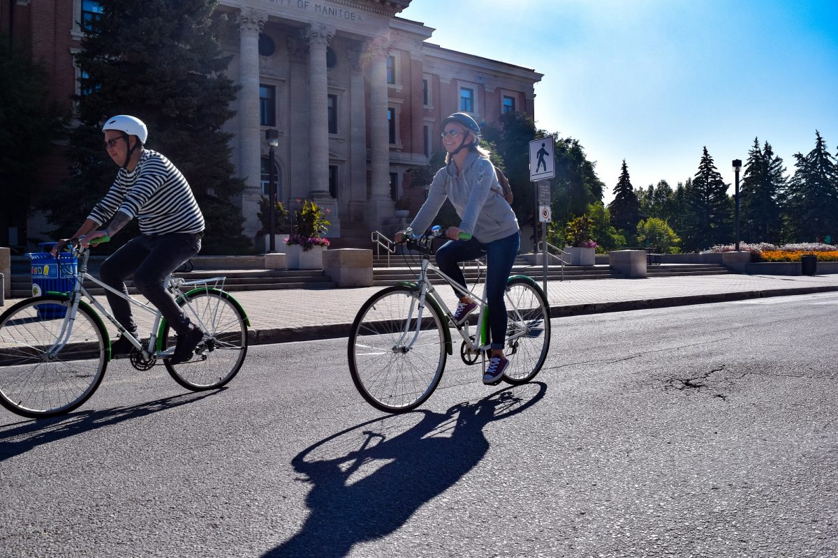 Two people cycling past the Administrative Building on a sunny day.