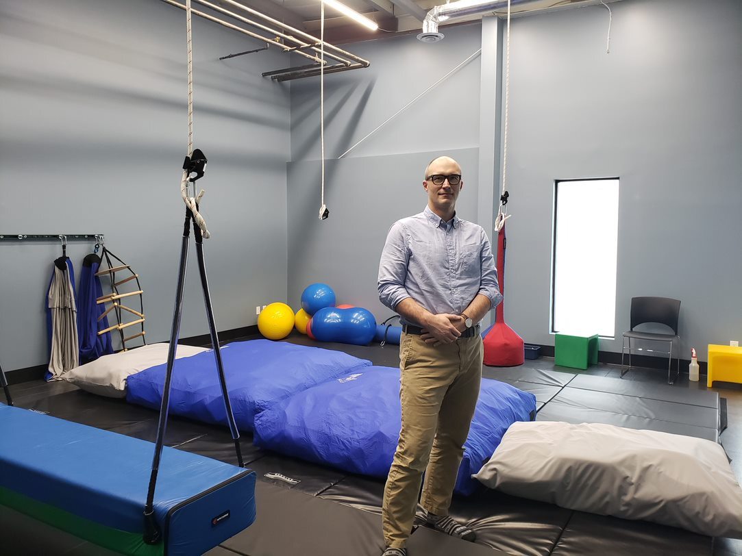 David Ambrose poses in his play therapy clinic, with gym mats and colourful balls behind him.