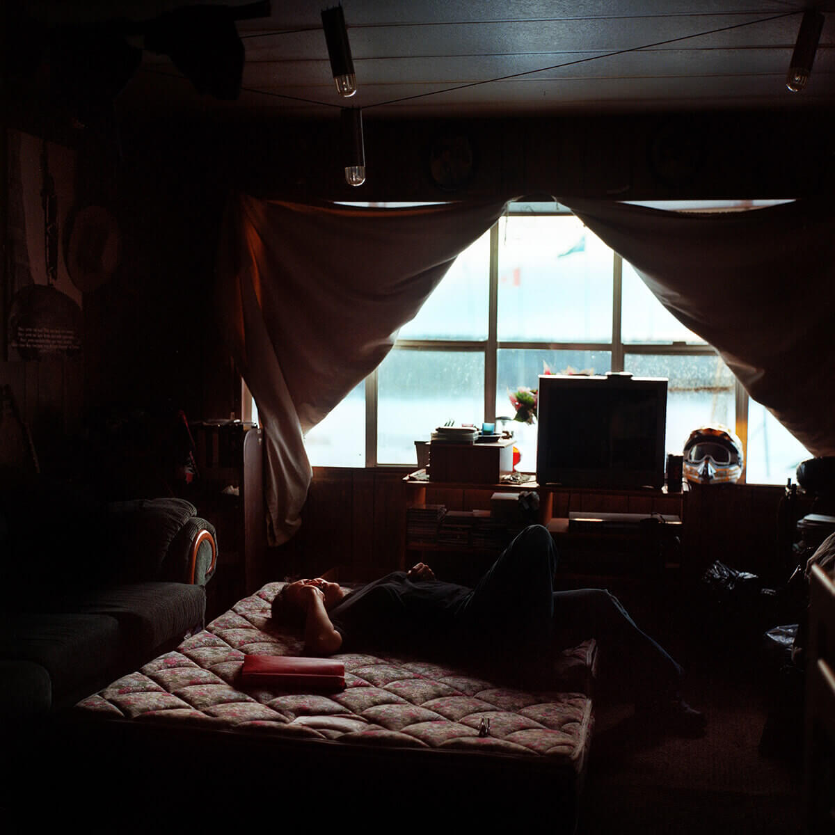 A photo of a Cree truck driver resting on a bare mattress in a cabin.